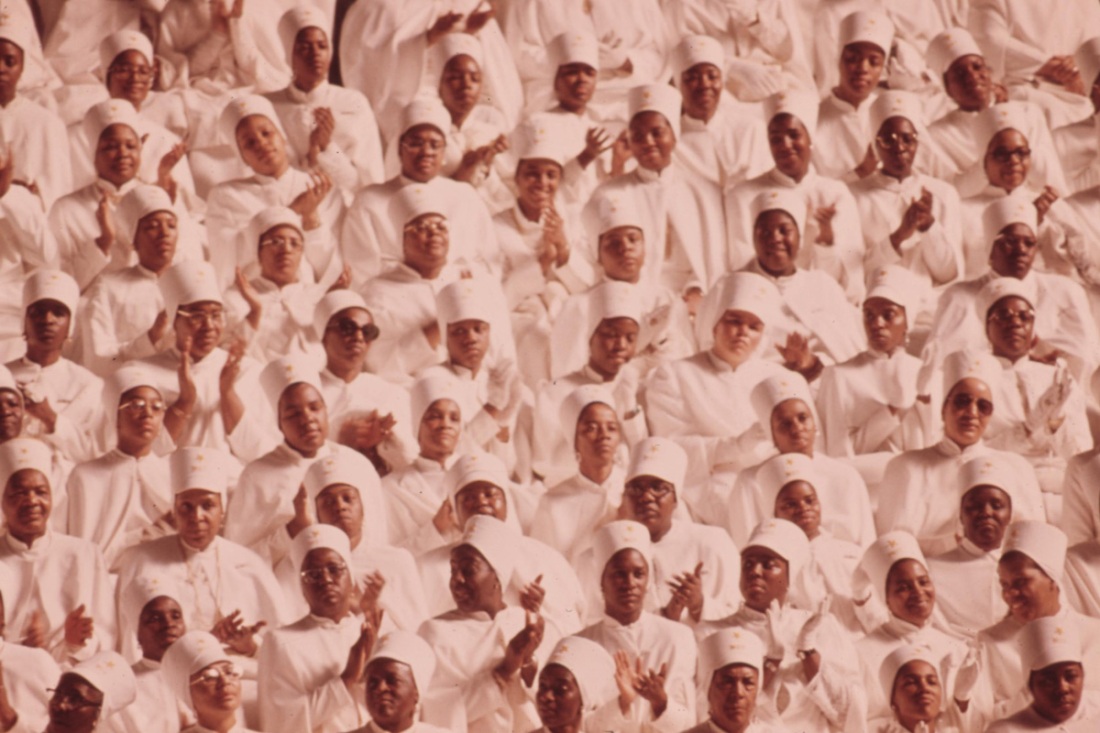 Black muslim women dressed In white applaud Elijah Muhammad during the delivery of his annual savior's day message In Chicago.