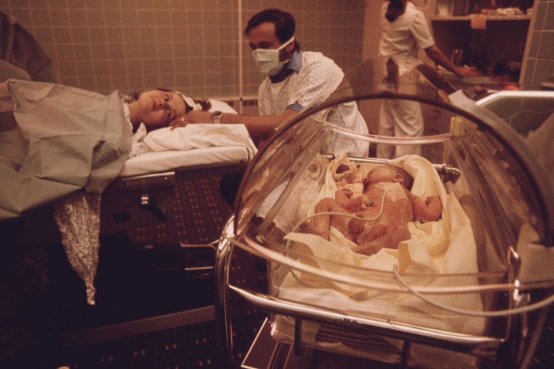 Woman who has just given birth in the delivery room of Loretto hospital in New Ulm, Minnesota. Her husband, who observed the birth, holds his wife's head as she turns to gaze at her newborn child.